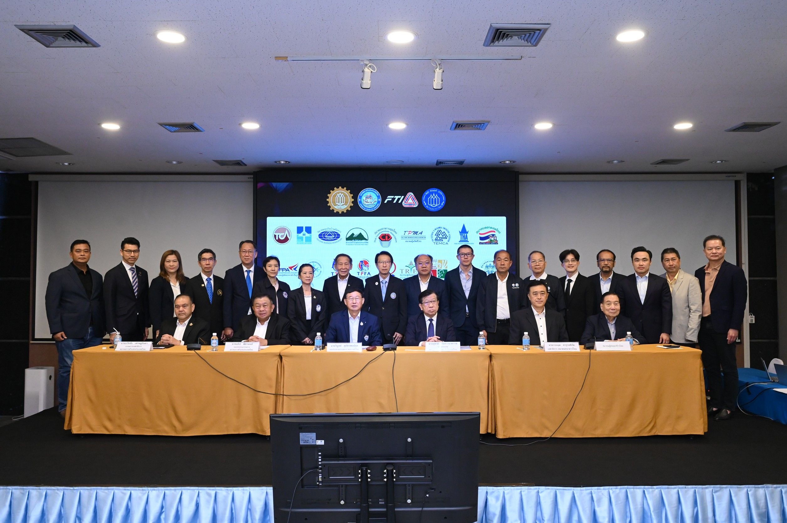 Business professionals gather in a conference room, some seated at a long table.