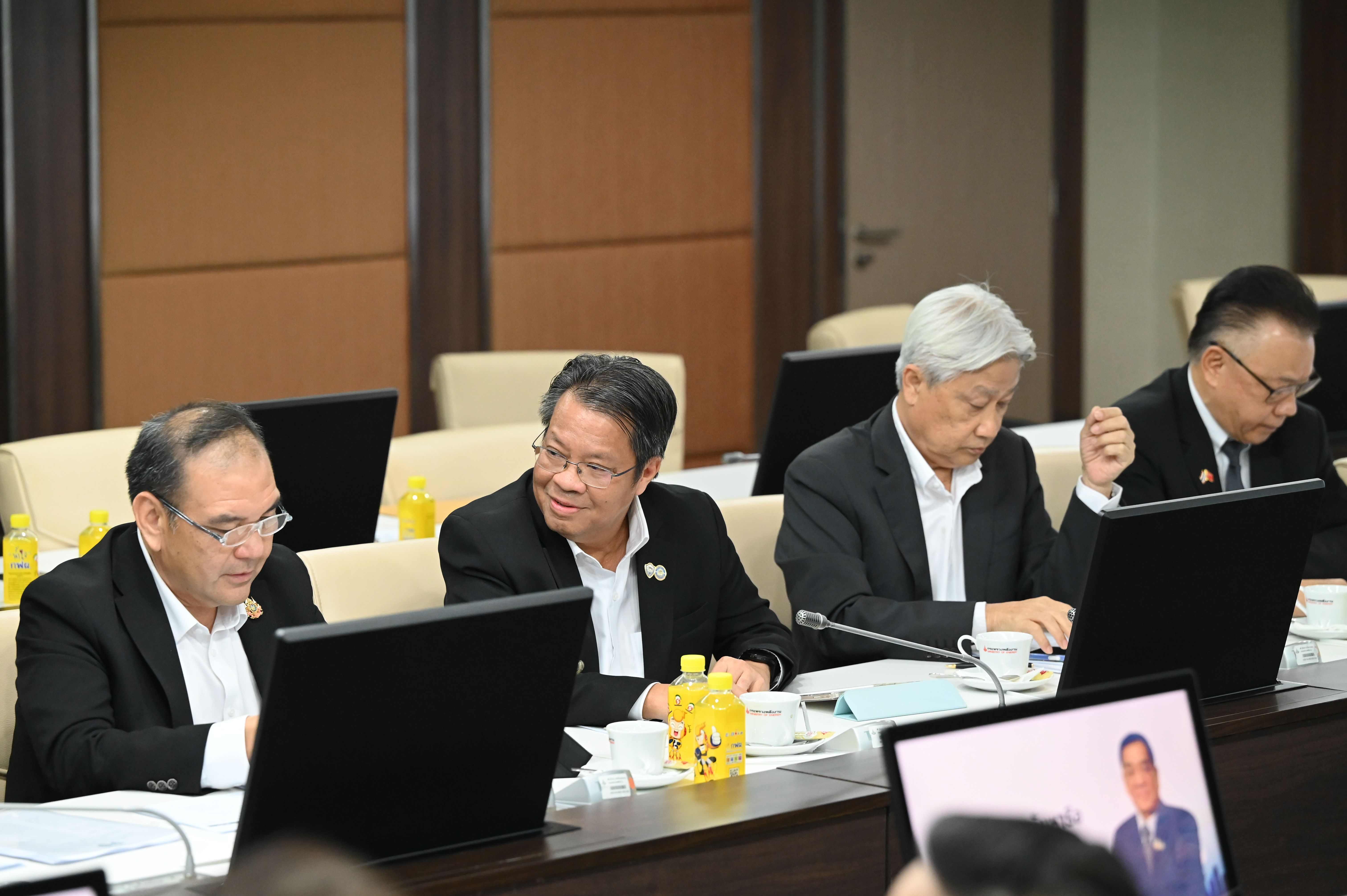 Four men in dark suits attend a meeting around a conference table with laptops.
