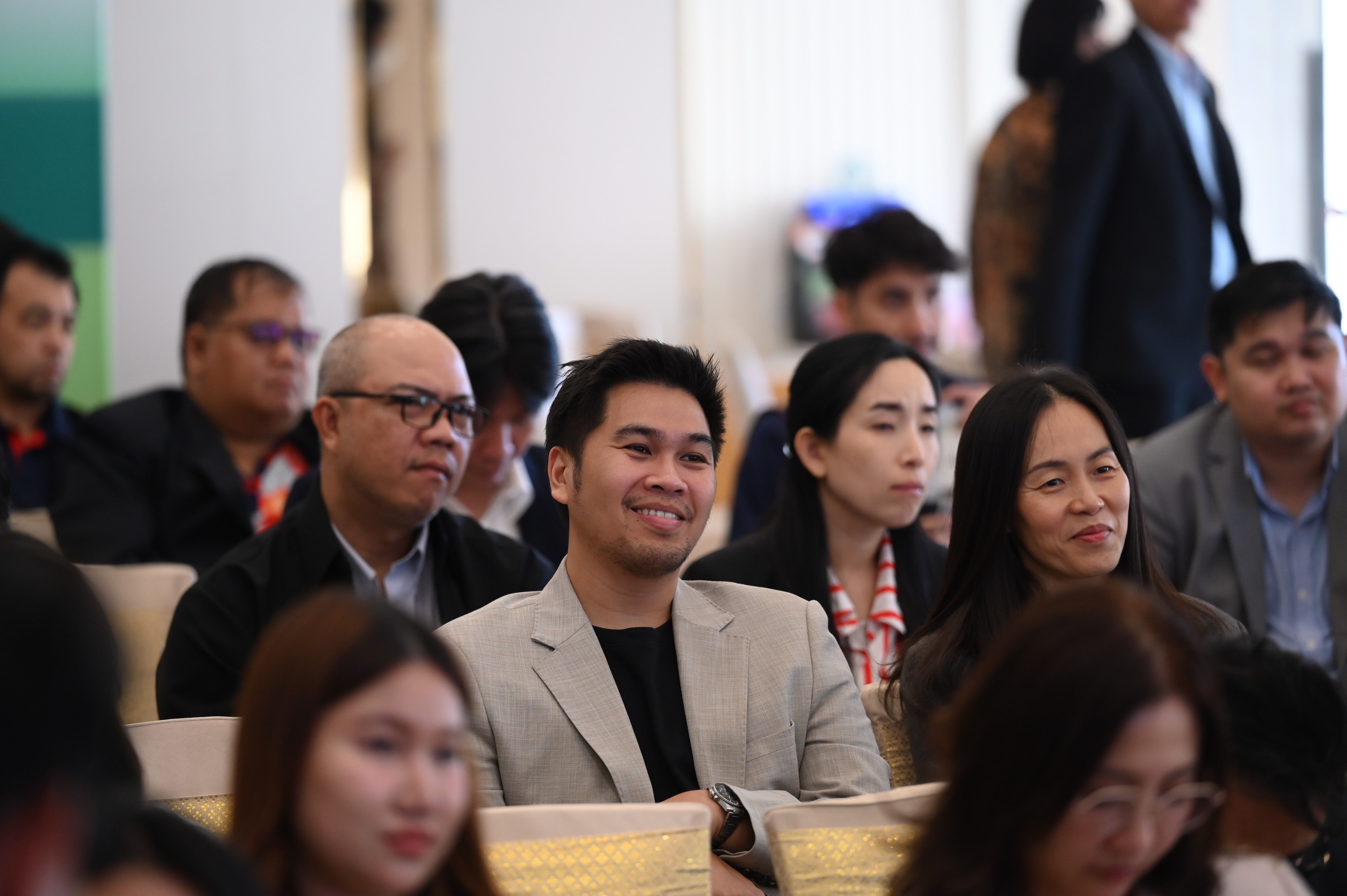 A man in a light suit jacket smiles while attending a professional meeting.