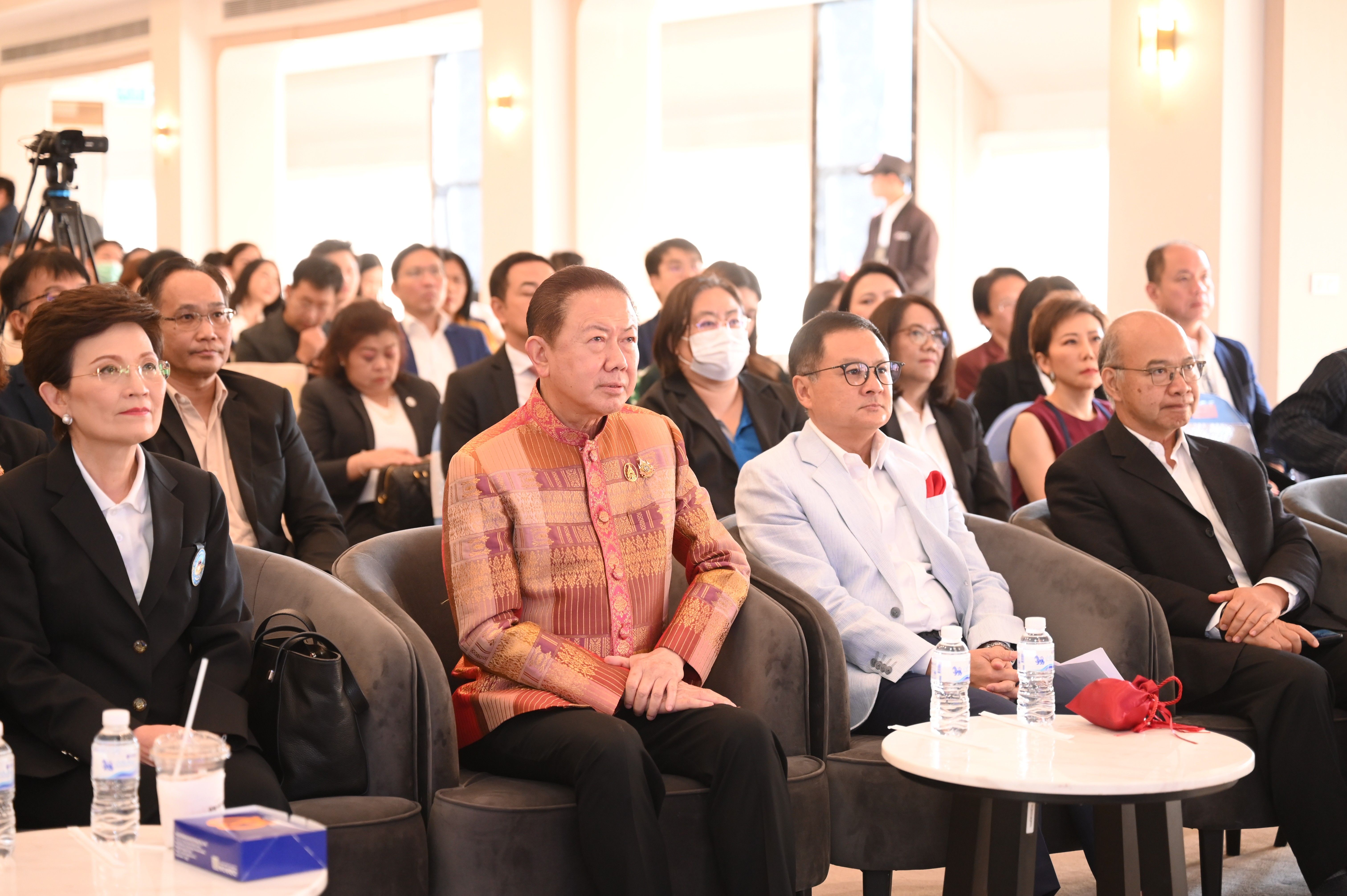 Distinguished attendees, including men and women, are seated and listening at an indoor conference event.