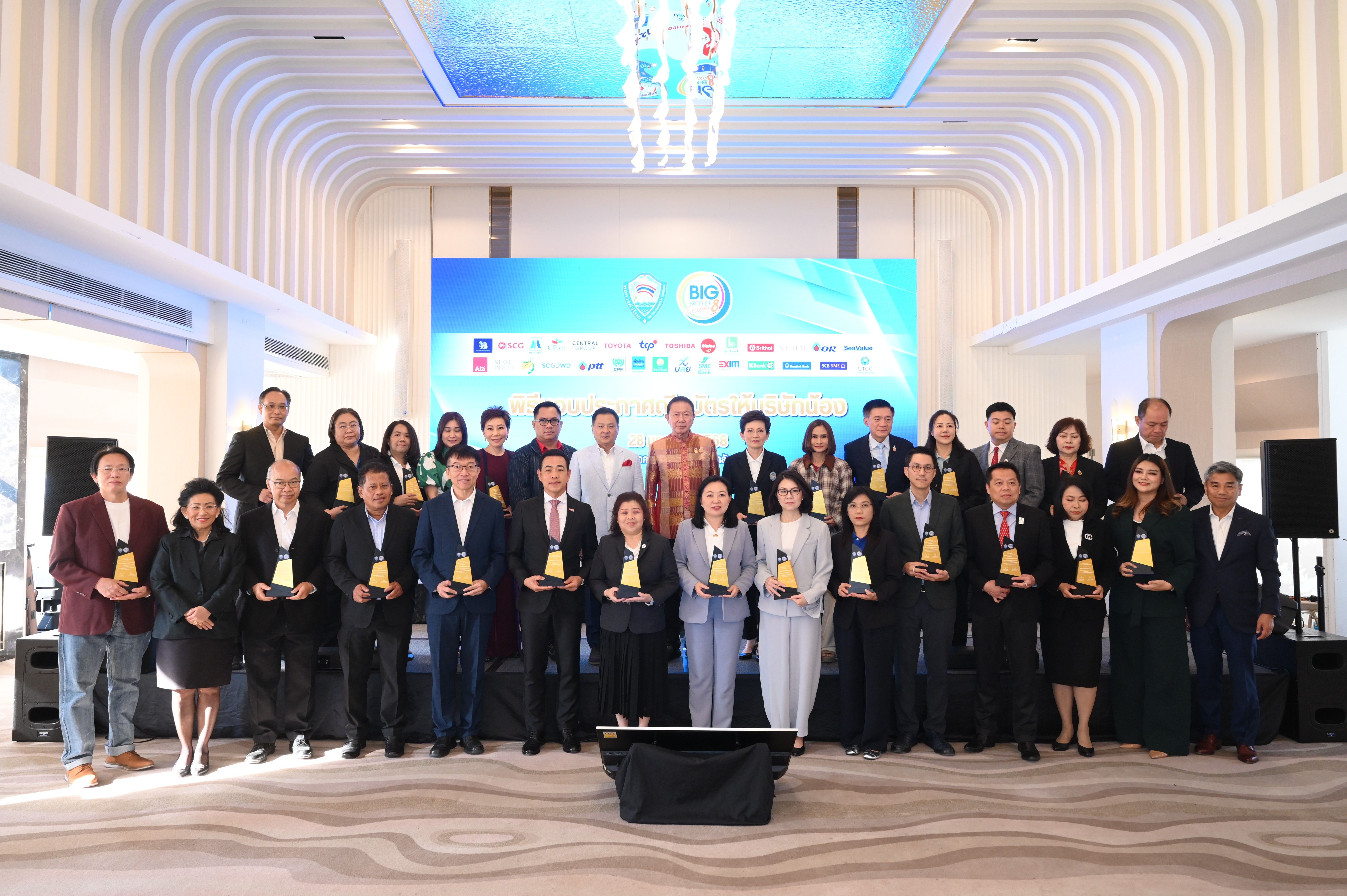 A large group of formally dressed people proudly hold golden awards at a corporate ceremony.