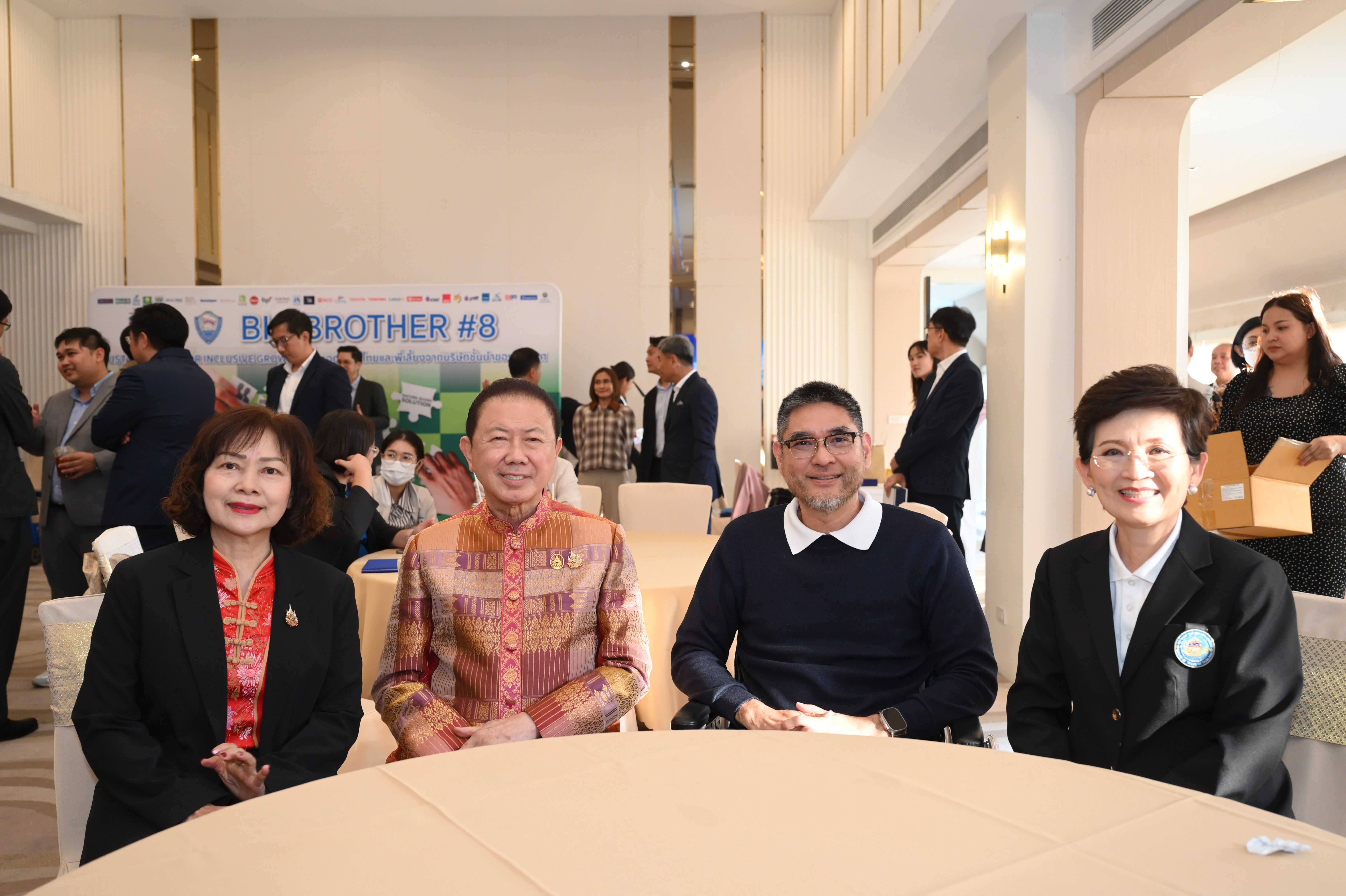 Four smiling people, two men and two women, sit at a table during an event.