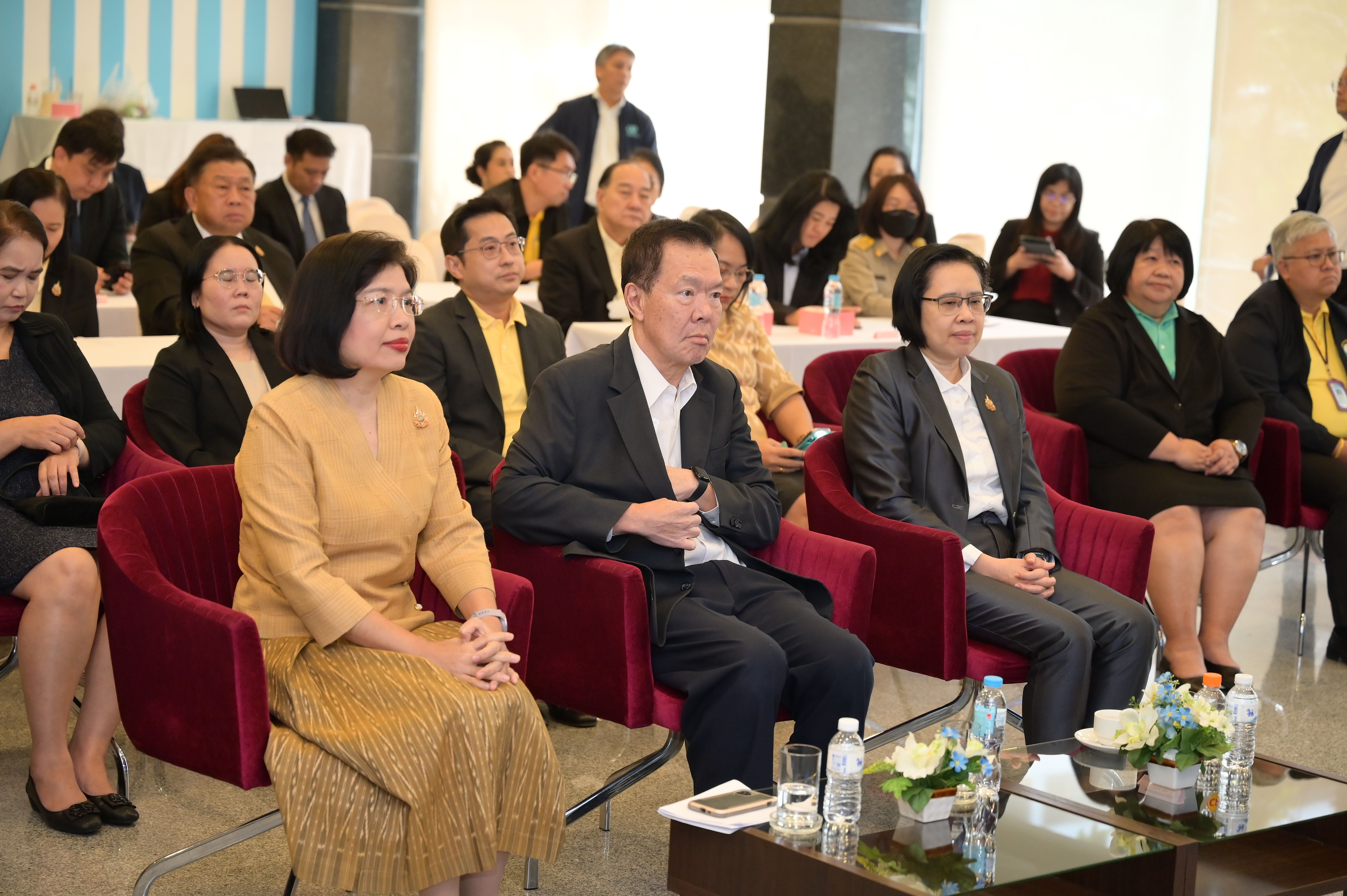 Attendees in formal attire sit in rows, observing an event in a conference setting.