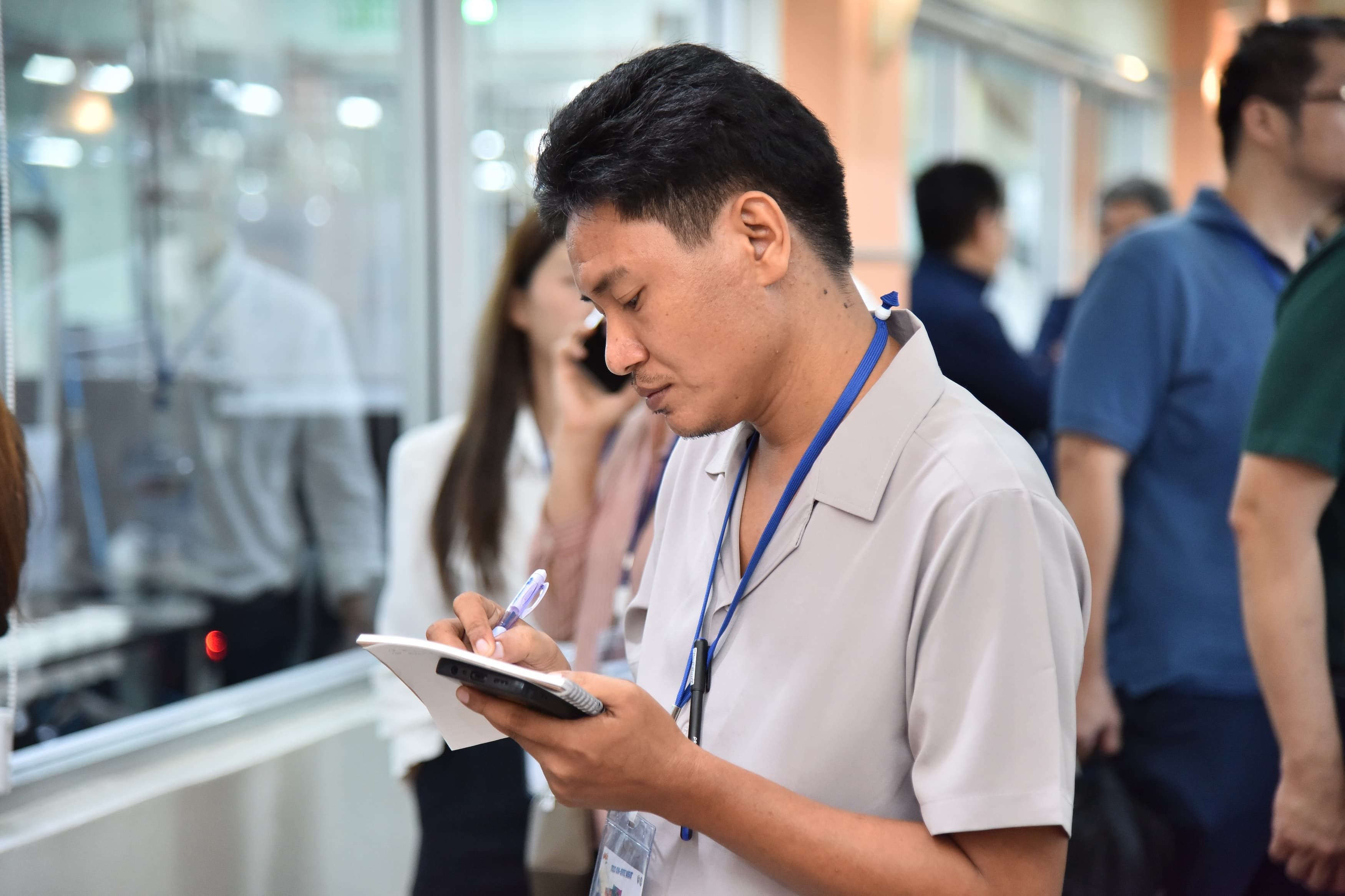 Man in light shirt writing notes in a small notebook with a pen at an event.