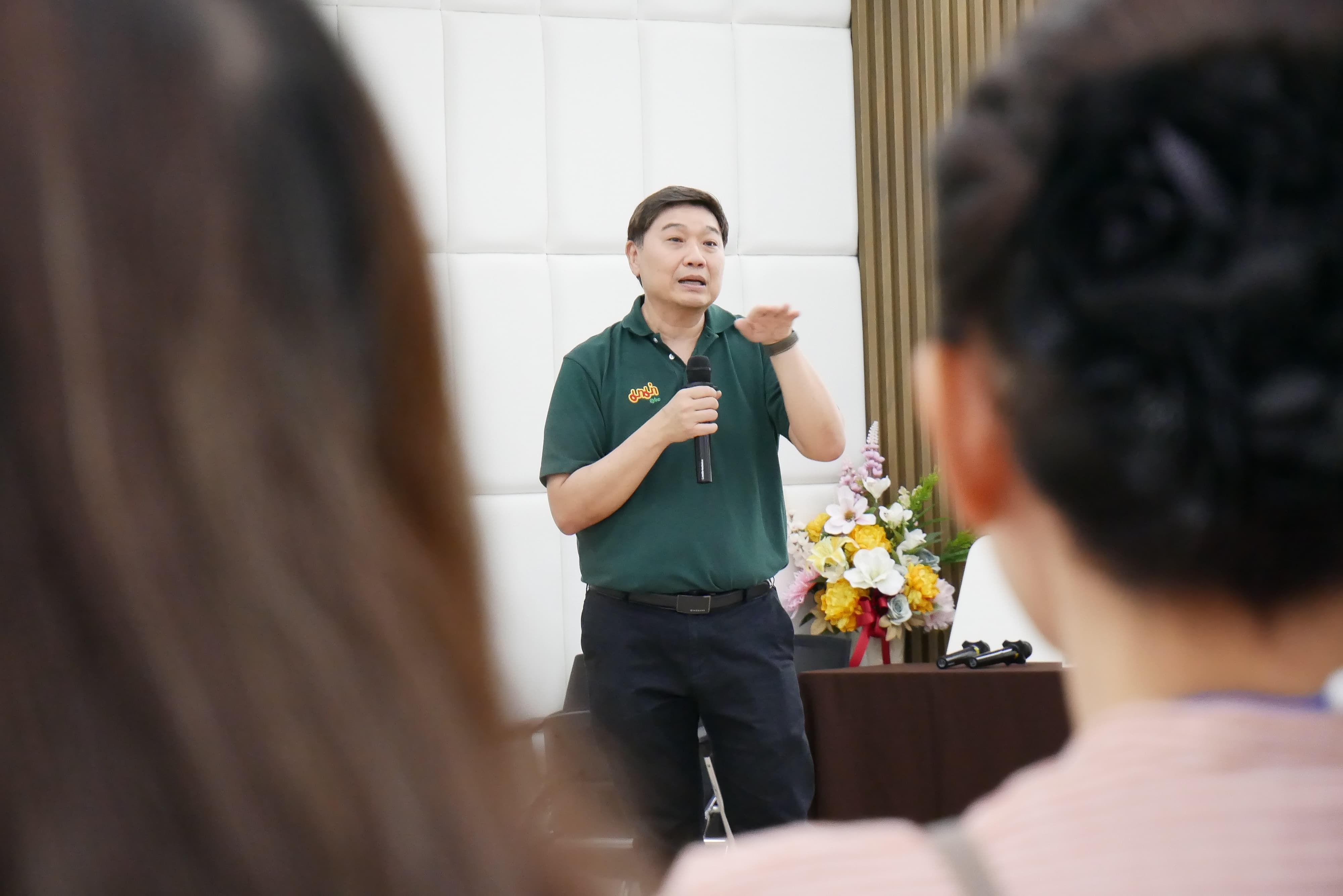 Man in green polo shirt speaks to an audience, gesturing with his hands during a presentation.