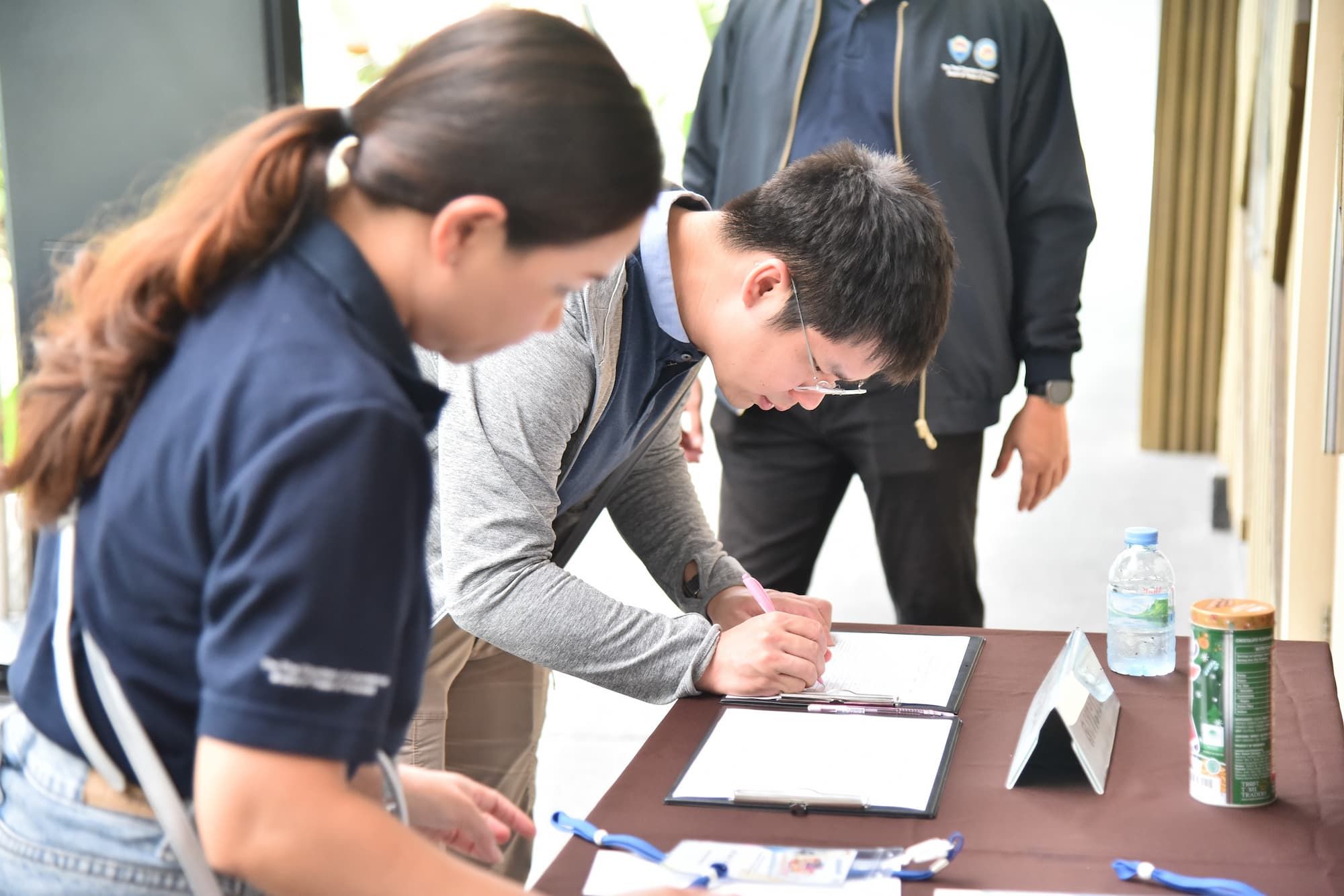 A woman watches a man sign a document at a registration table.