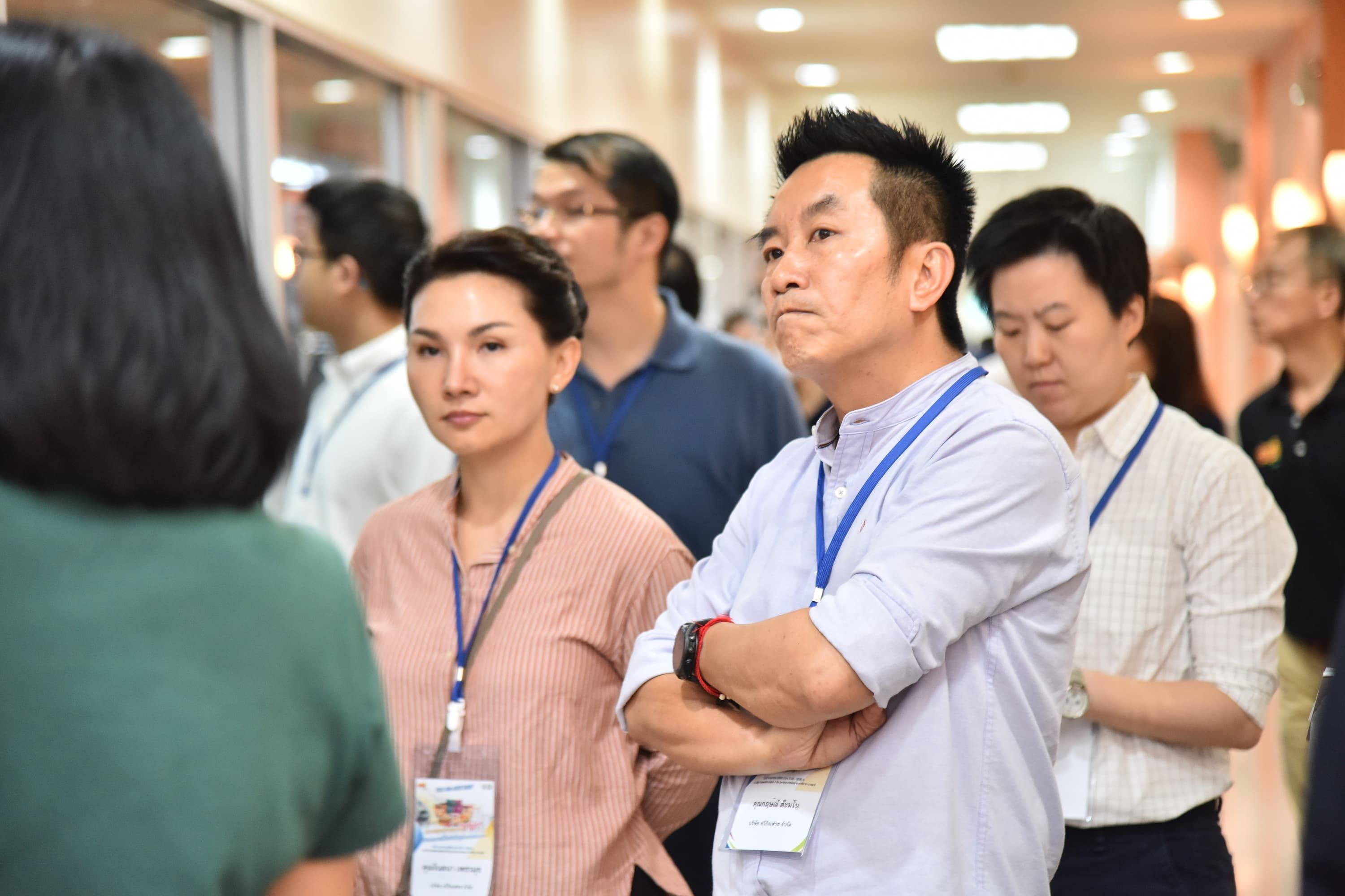 Two professionals with lanyards observe an event, man with crossed arms.