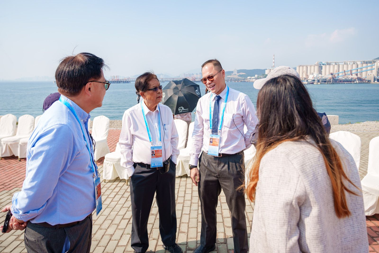 Four professionals chat by the water with distant buildings under a clear sky.