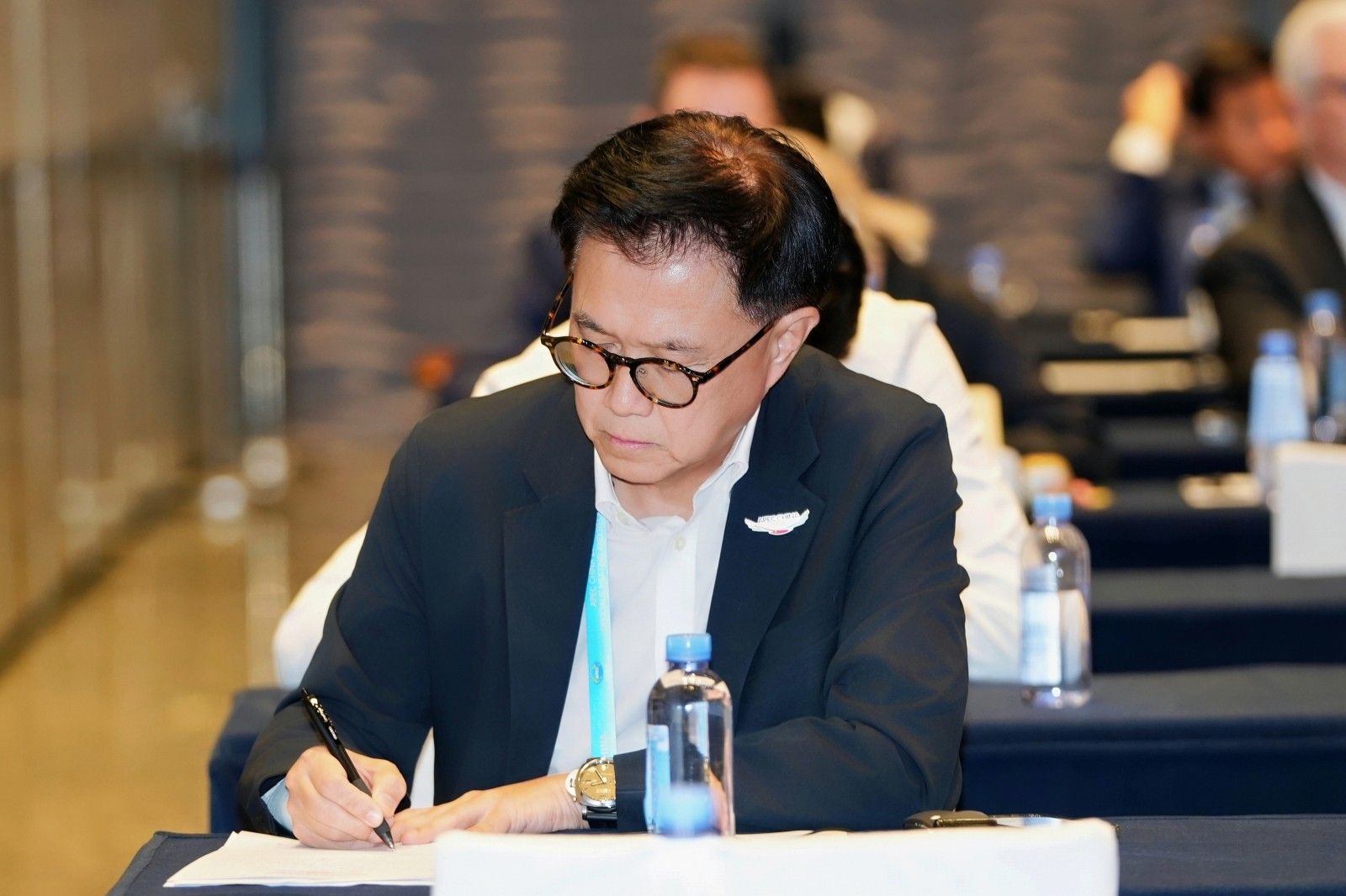 Man in glasses intently writing notes with a pen at a conference table.