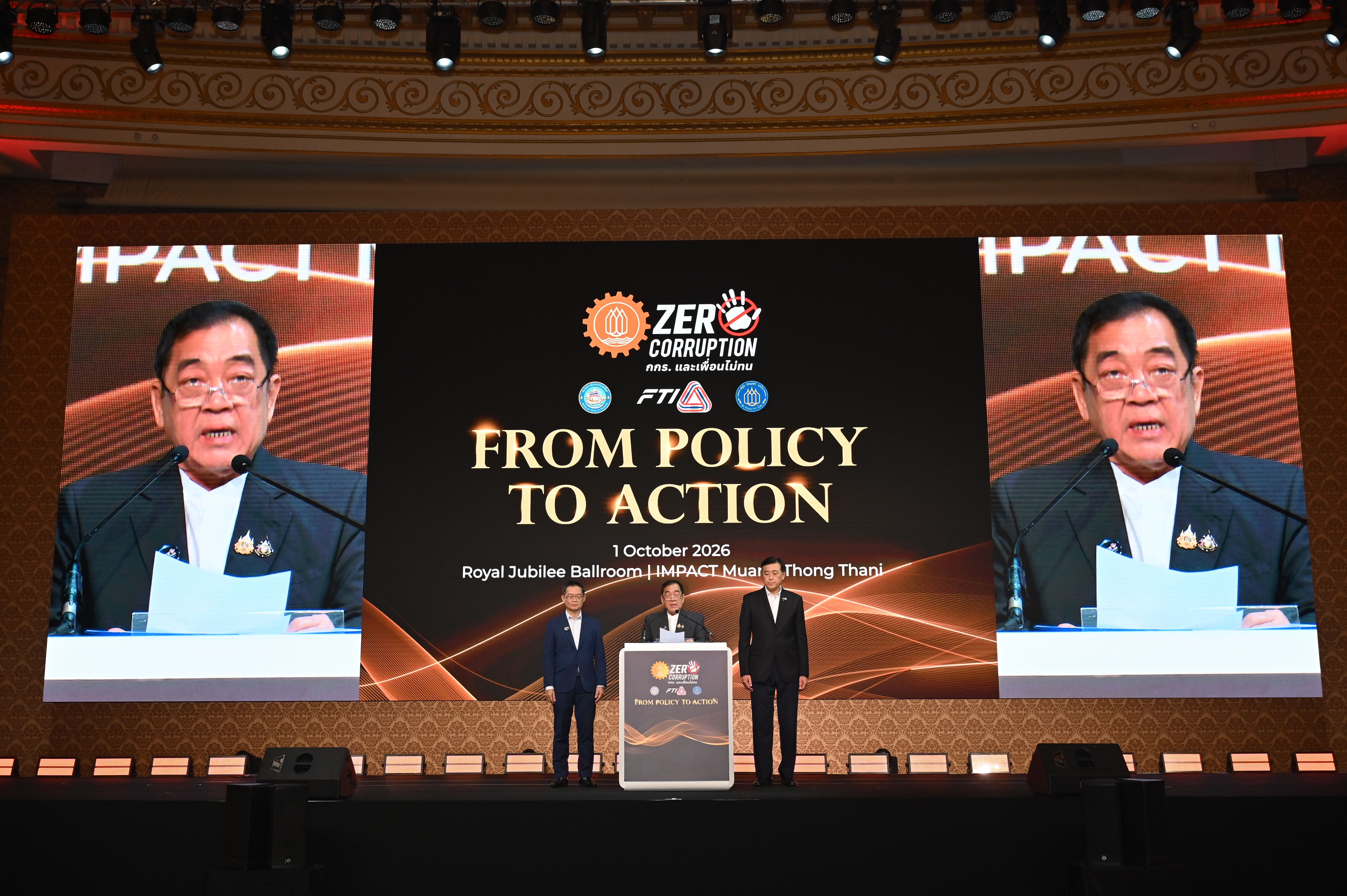 Three men on stage below a screen displaying 'FROM POLICY TO ACTION' at a conference.