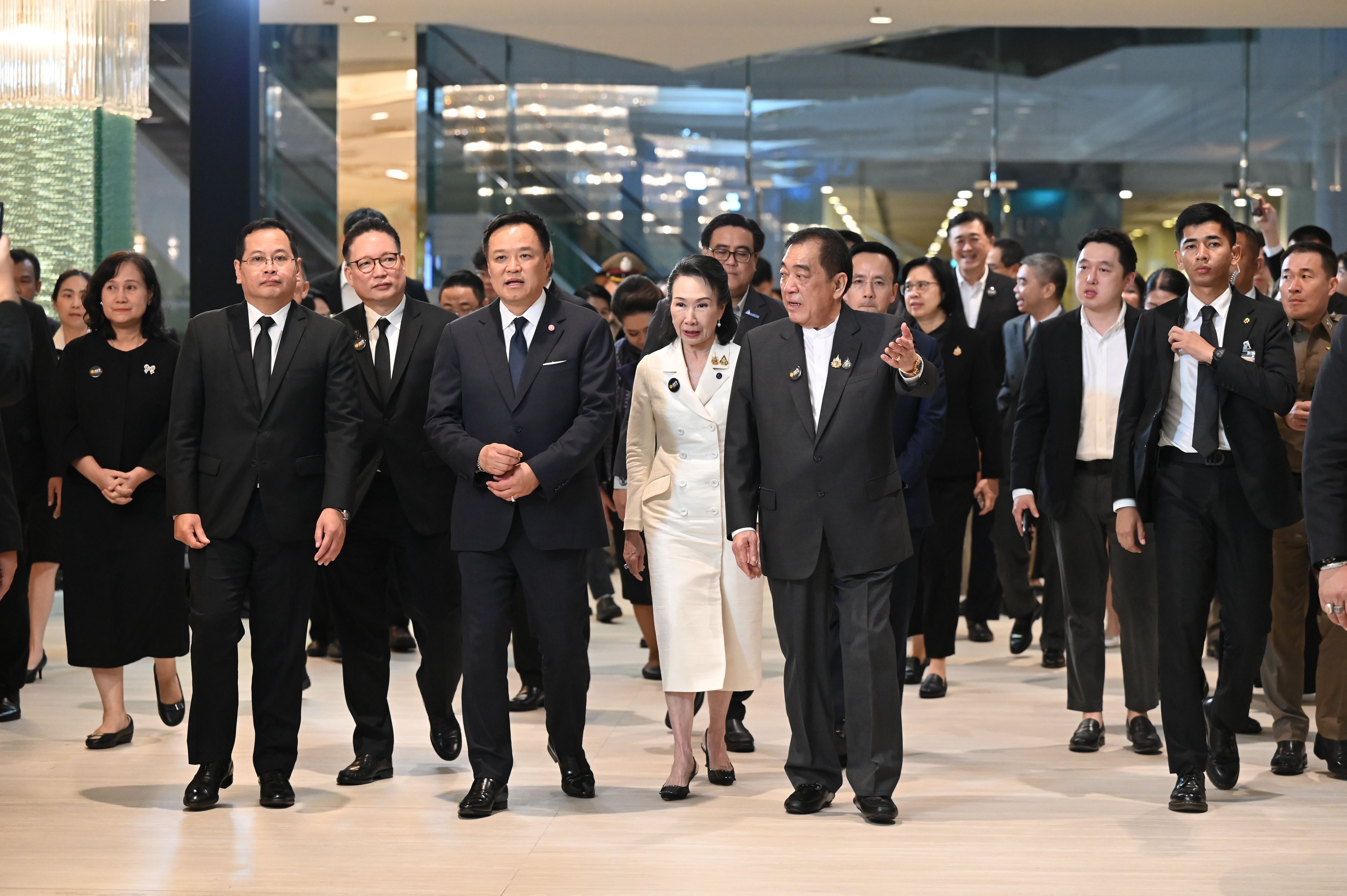 Formally dressed officials and dignitaries walk through a brightly lit modern building interior.