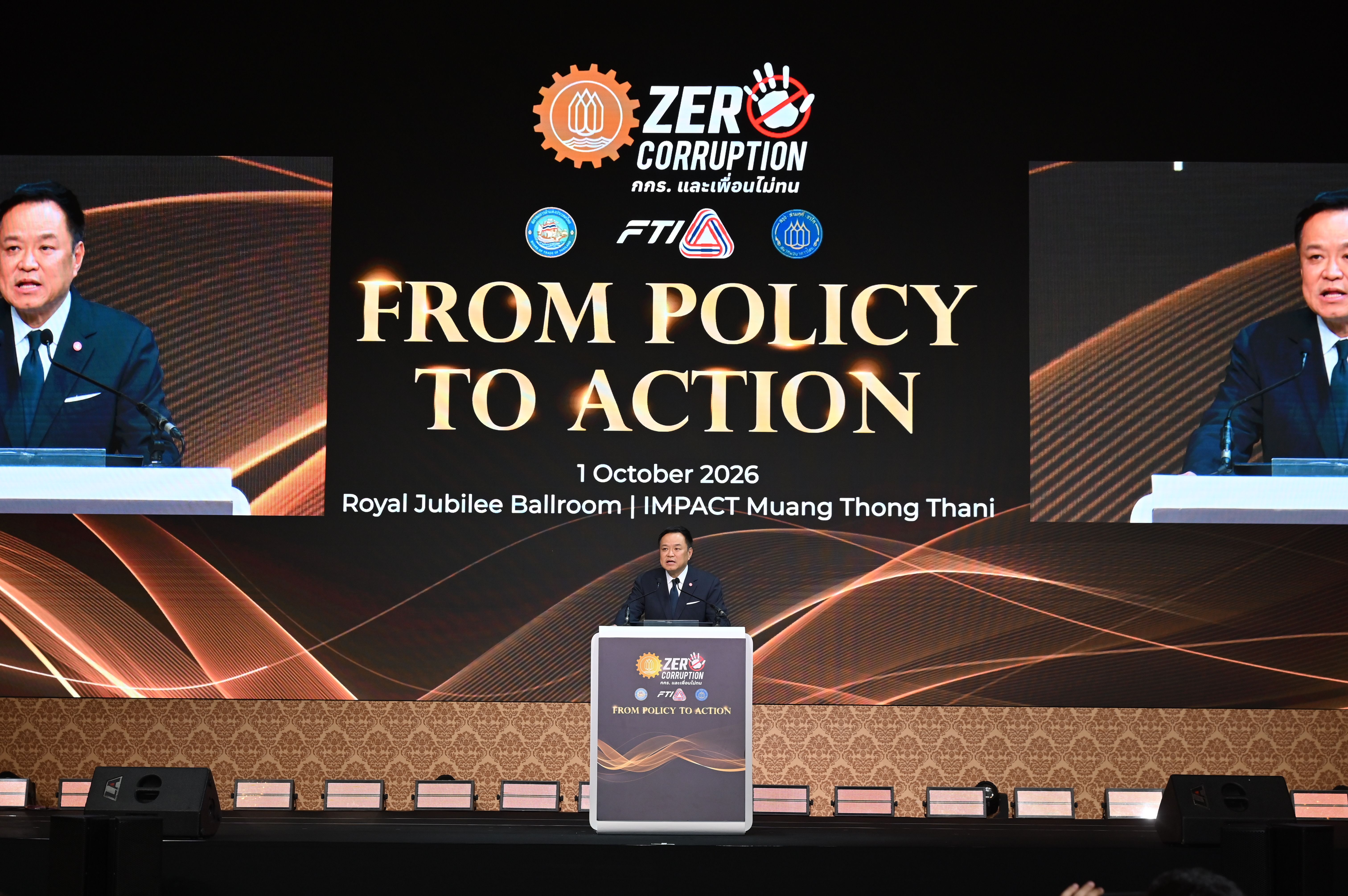 Conference speaker at a podium, large screen reads 'ZERO CORRUPTION FROM POLICY TO ACTION'.