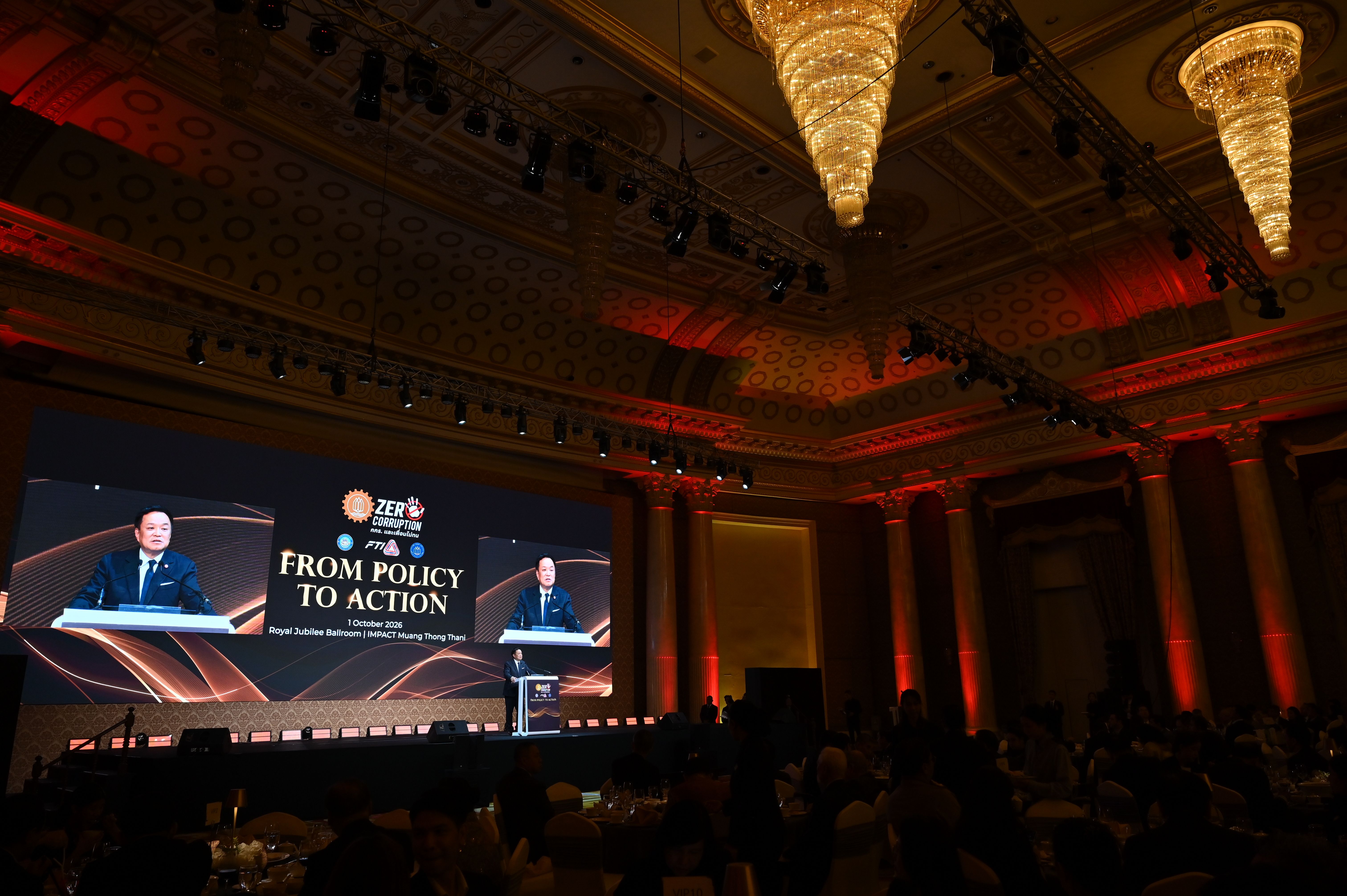 A speaker presents on a large screen at a conference, displaying 'FROM POLICY TO ACTION'.