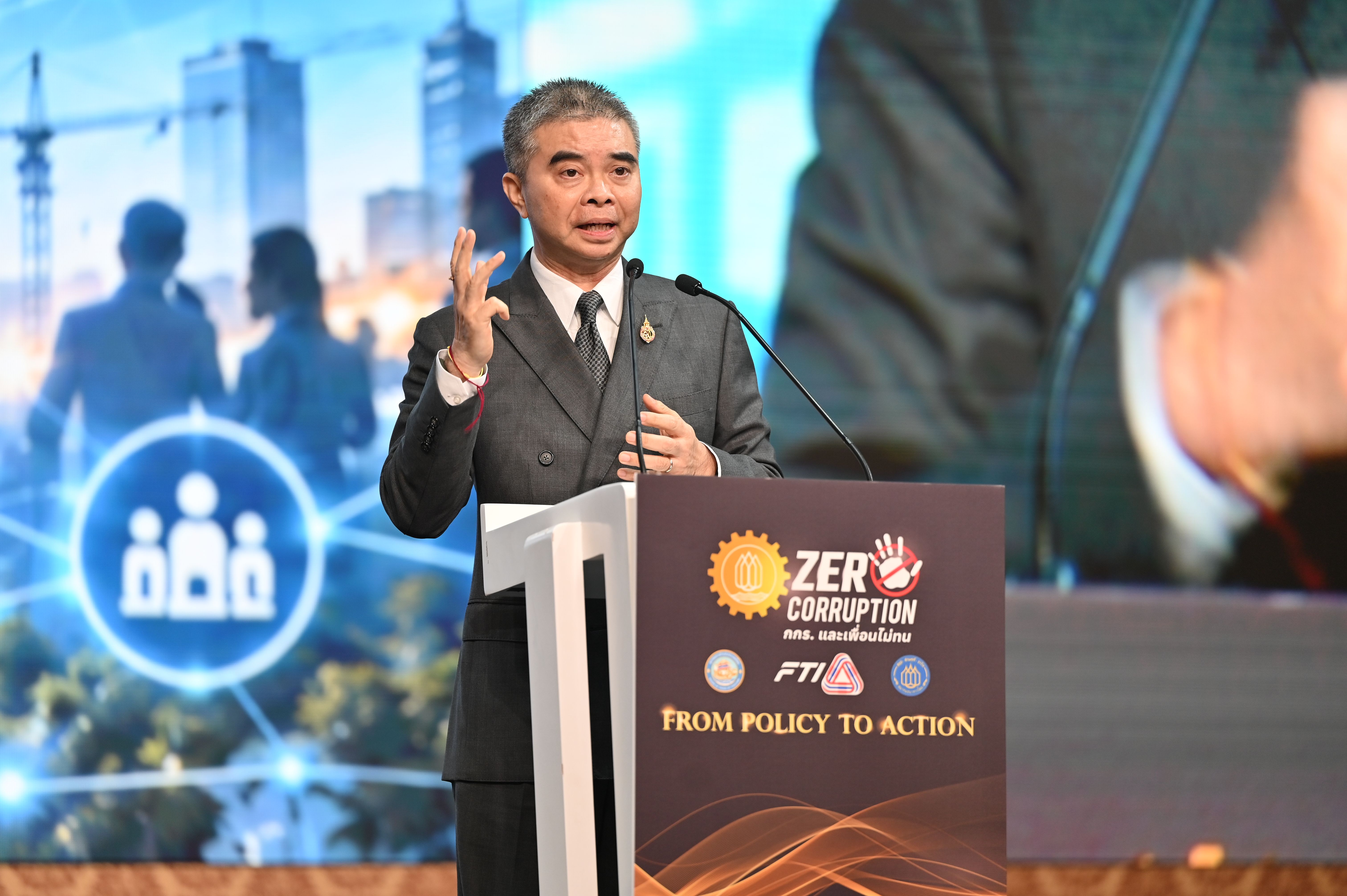 Man in suit speaking and gesturing at a podium with 'Zero Corruption' branding.
