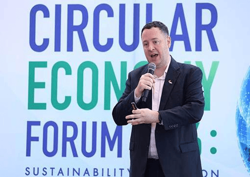 Man speaking into a microphone at a 'Circular Economy Forum' event.
