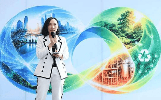 Woman in white suit speaking at podium with sustainability graphic background.