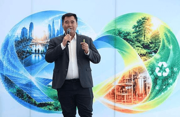 A man speaks on stage before a dynamic backdrop showing urban development and natural environments.