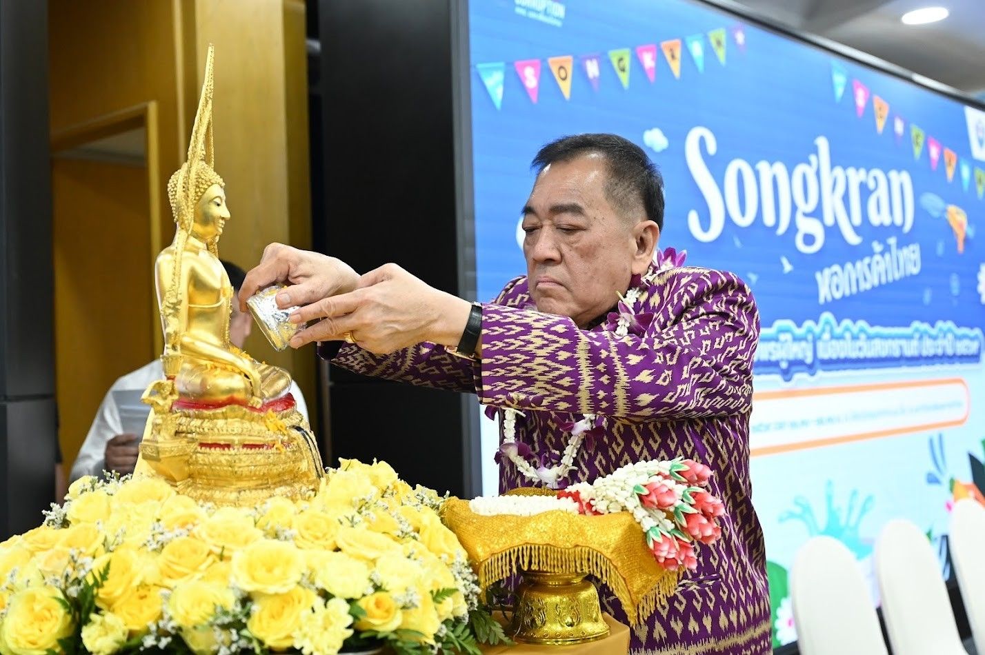 An older man pours water over a golden Buddha statue, dressed in traditional attire.