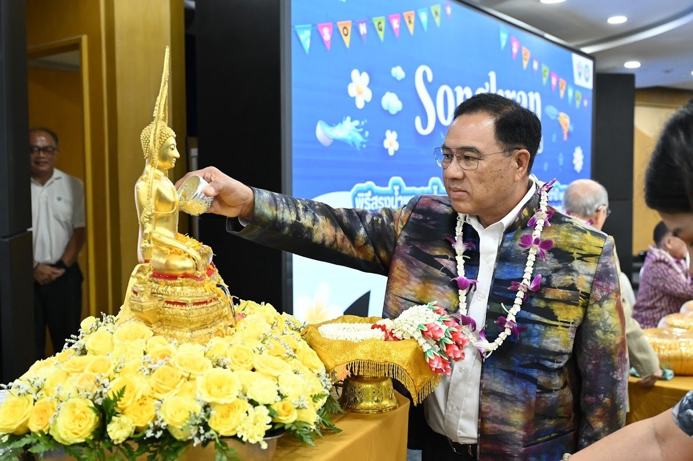 A man in a colorful shirt pours water over a golden Buddha statue.