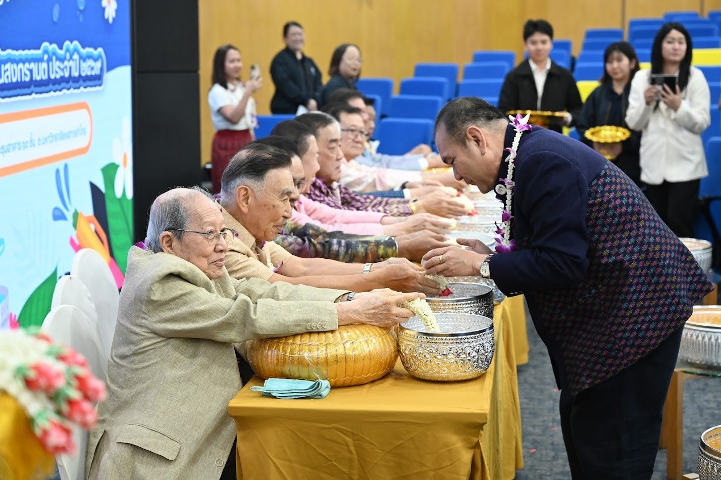 A man pours water over the hands of an older man seated at a table.