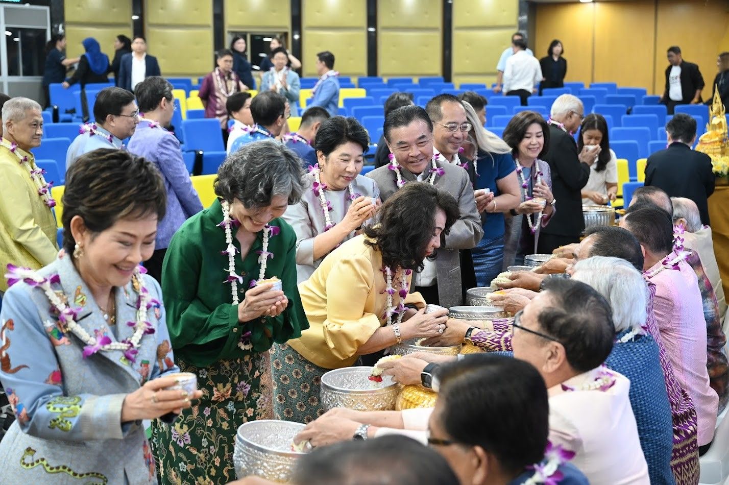 Many people, some wearing leis, participate in a water pouring ritual.