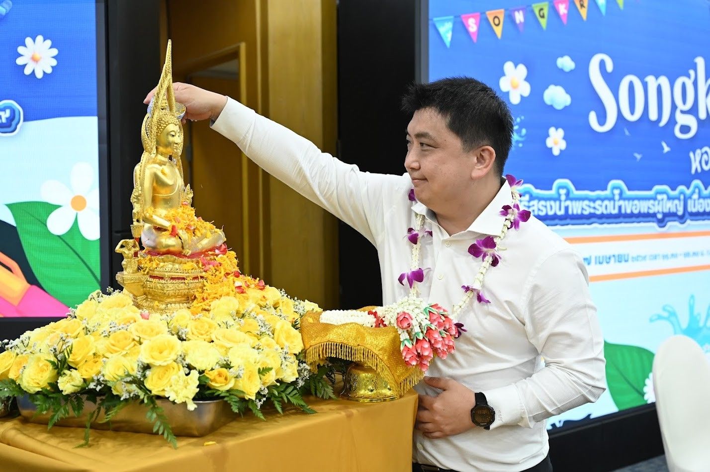 A man in a white shirt gently pours water over a golden Buddha statue.