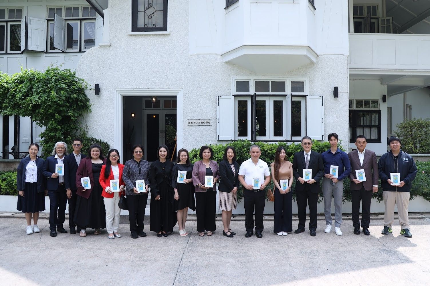 Diverse group holding small awards in front of a classic white building.