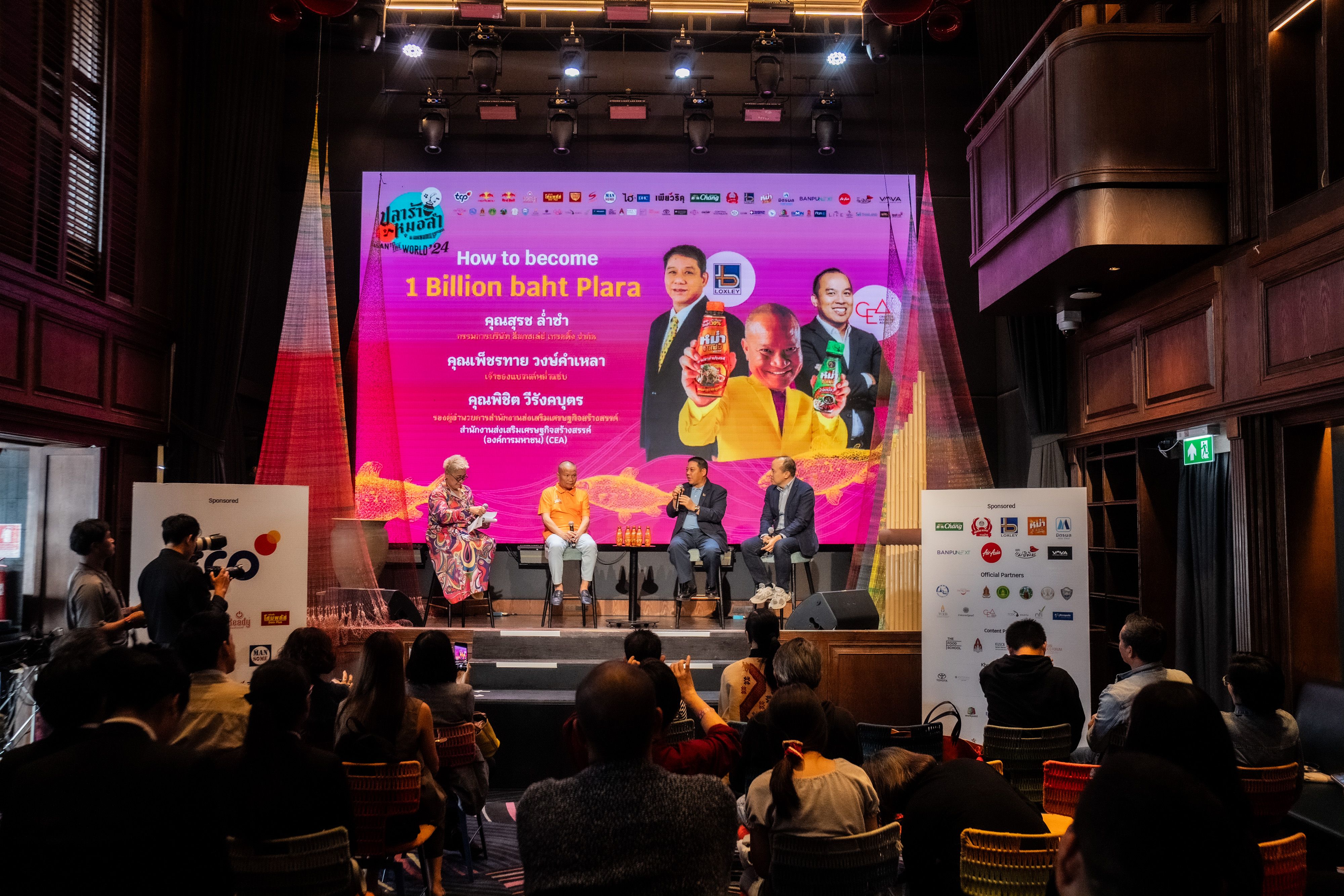 Five panelists on stage present during a discussion with a large screen display.