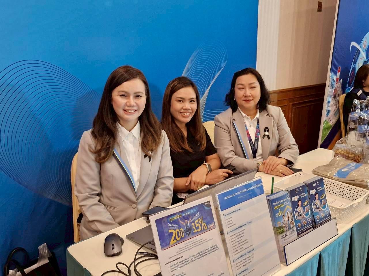 Three smiling women sit behind a booth table with promotional materials at an event.