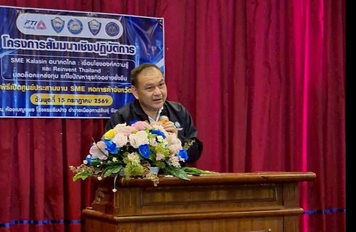 Man in suit speaking from a wooden podium with flowers at a conference event.